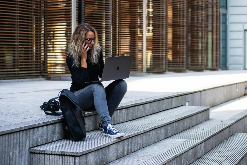 Woman sitting on steps using laptop and talking on phone