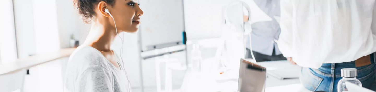 Woman working at bright office desk with laptop and earphones