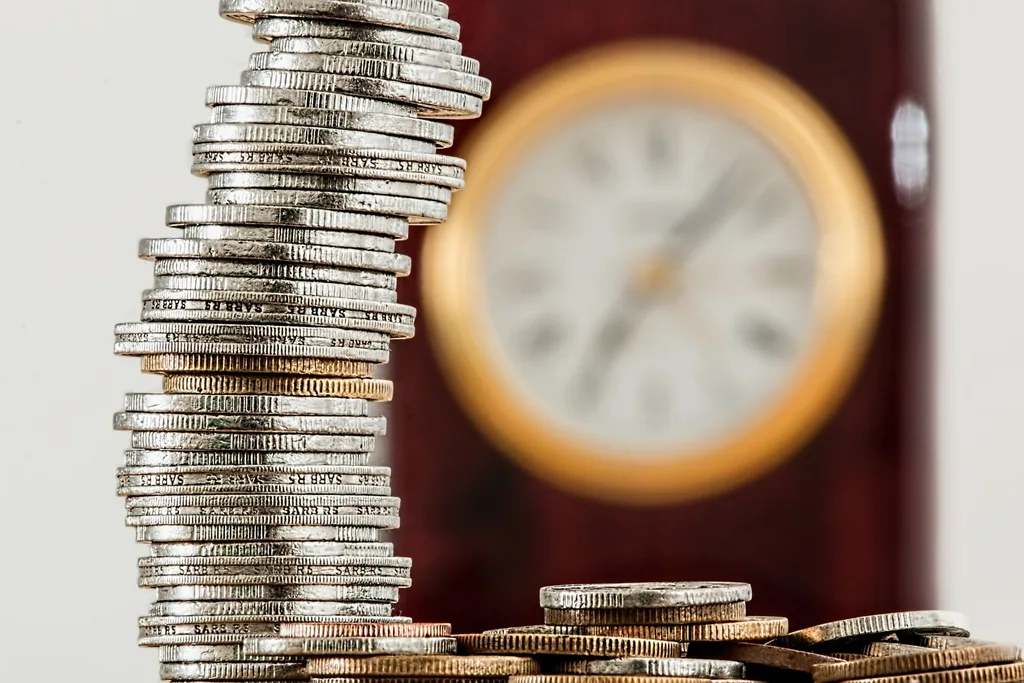 Stacked coins beside a clock showing financial value over time. 

