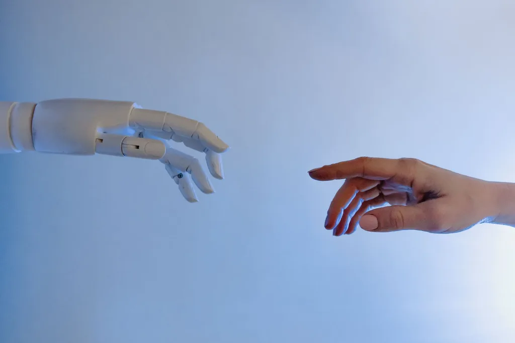 Human and robotic hands reaching out in workforce collaboration.